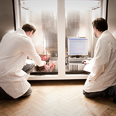 Two researchers in lab coats knelt on the floor, adjusting PC wires